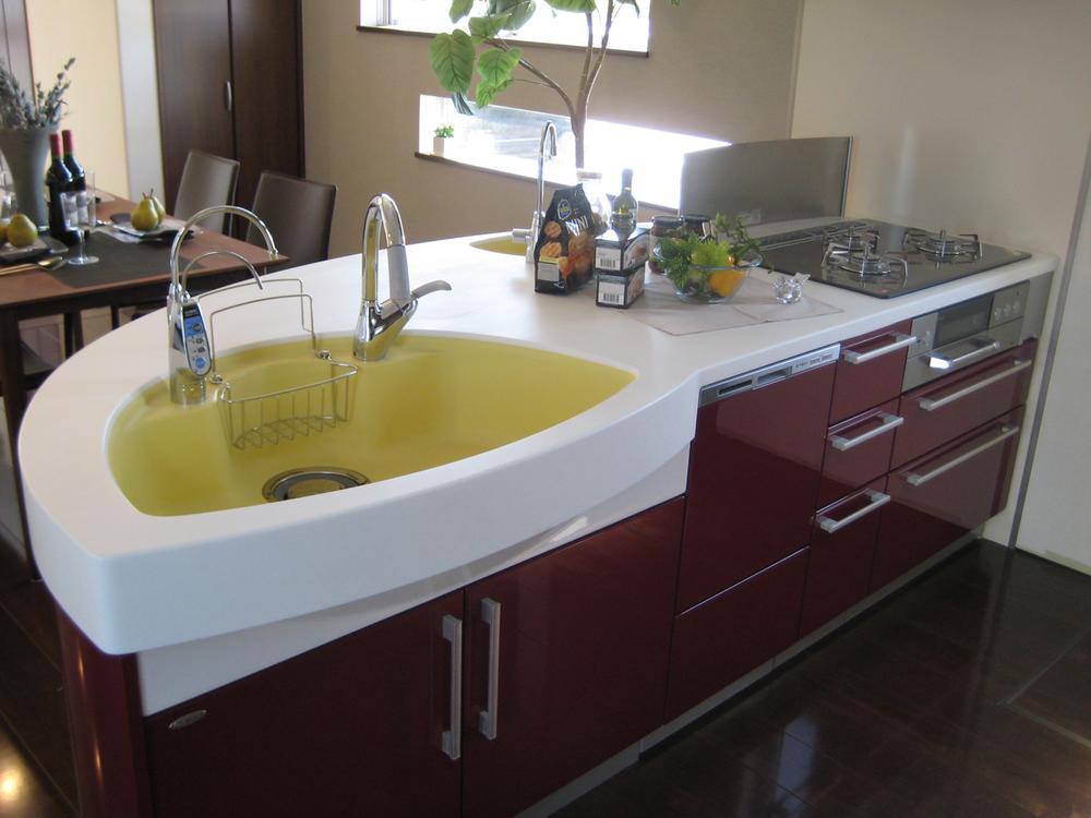 Kitchen.  [Model house kitchen] Red color is also impressive face-to-face system kitchen also shape. Facilities enhancement, such as dish washing dryer. Since the study corner also eye can reach from here, It is housework while watching the figure of children